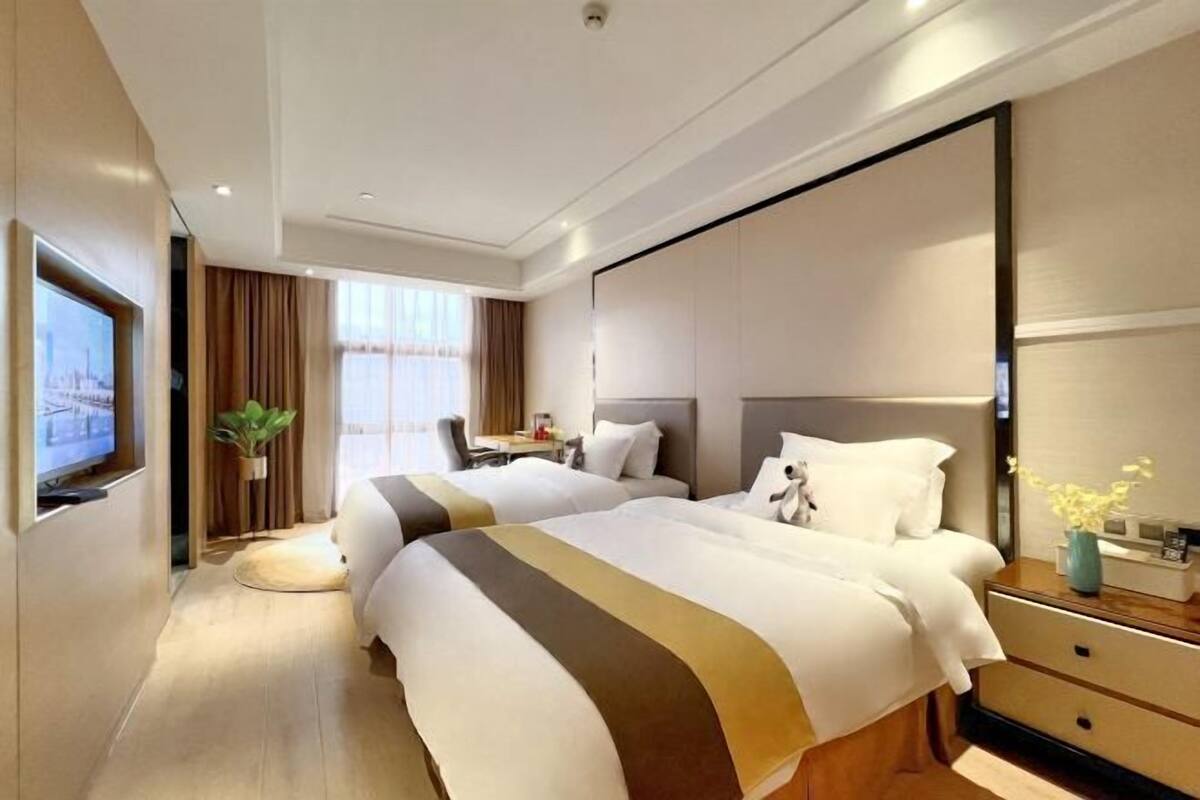 A hotel room with two beds, a television, a desk, and a large mirror.