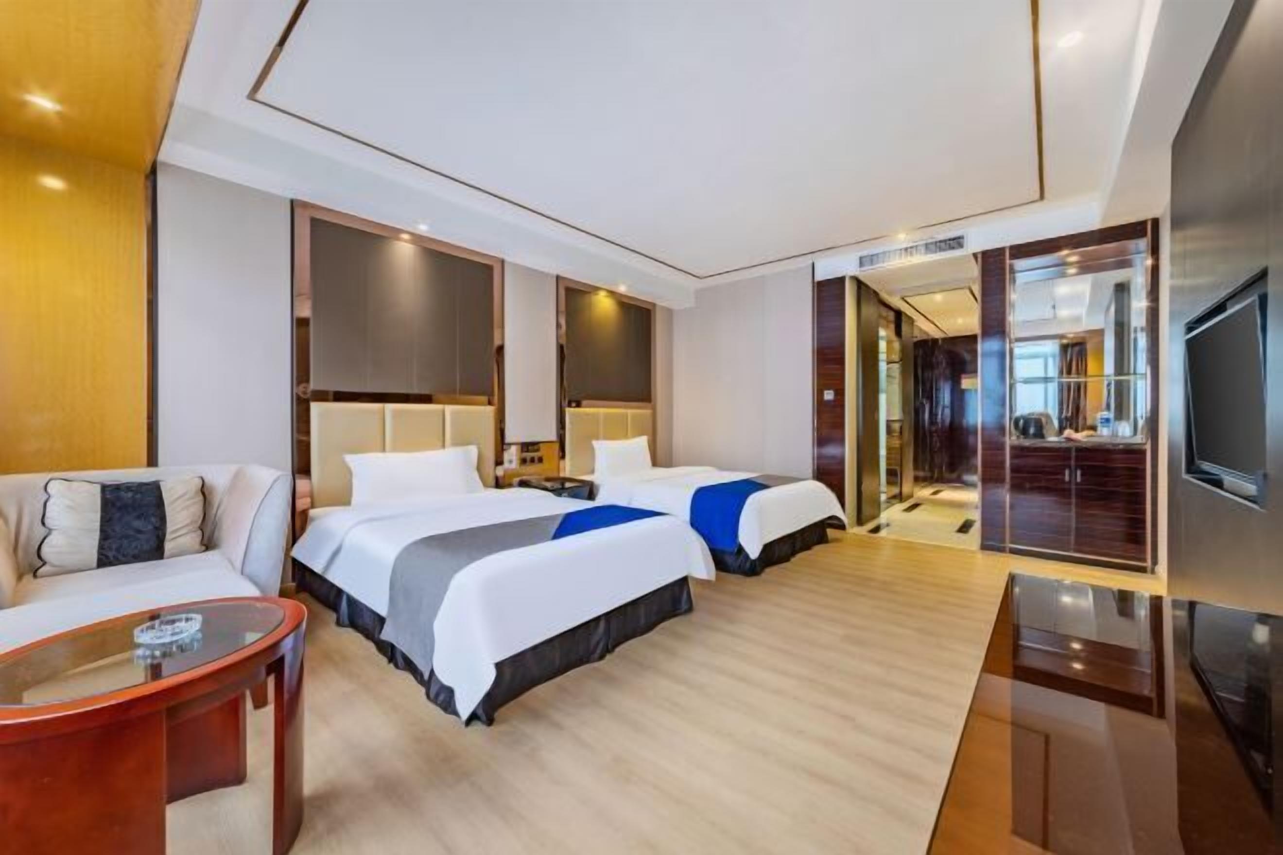 Una habitación de hotel moderna con dos camas, un sofá, un televisor y piso de madera.