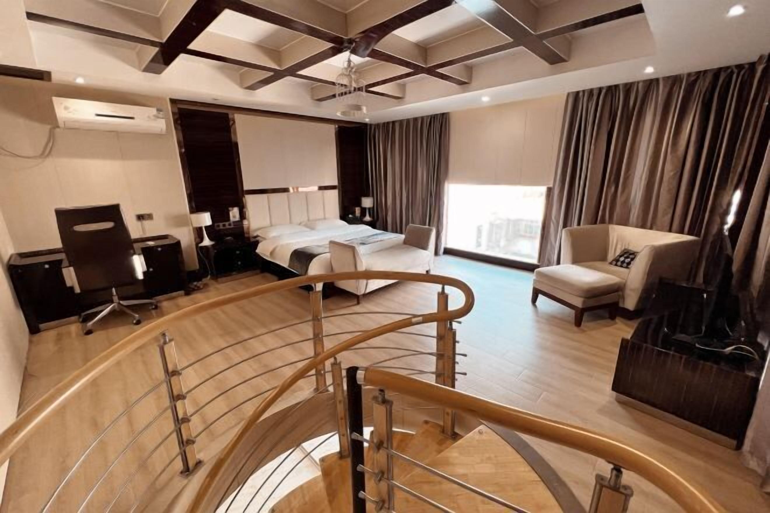 A modern hotel room with a curved staircase, a bed, a desk, and a seating area.