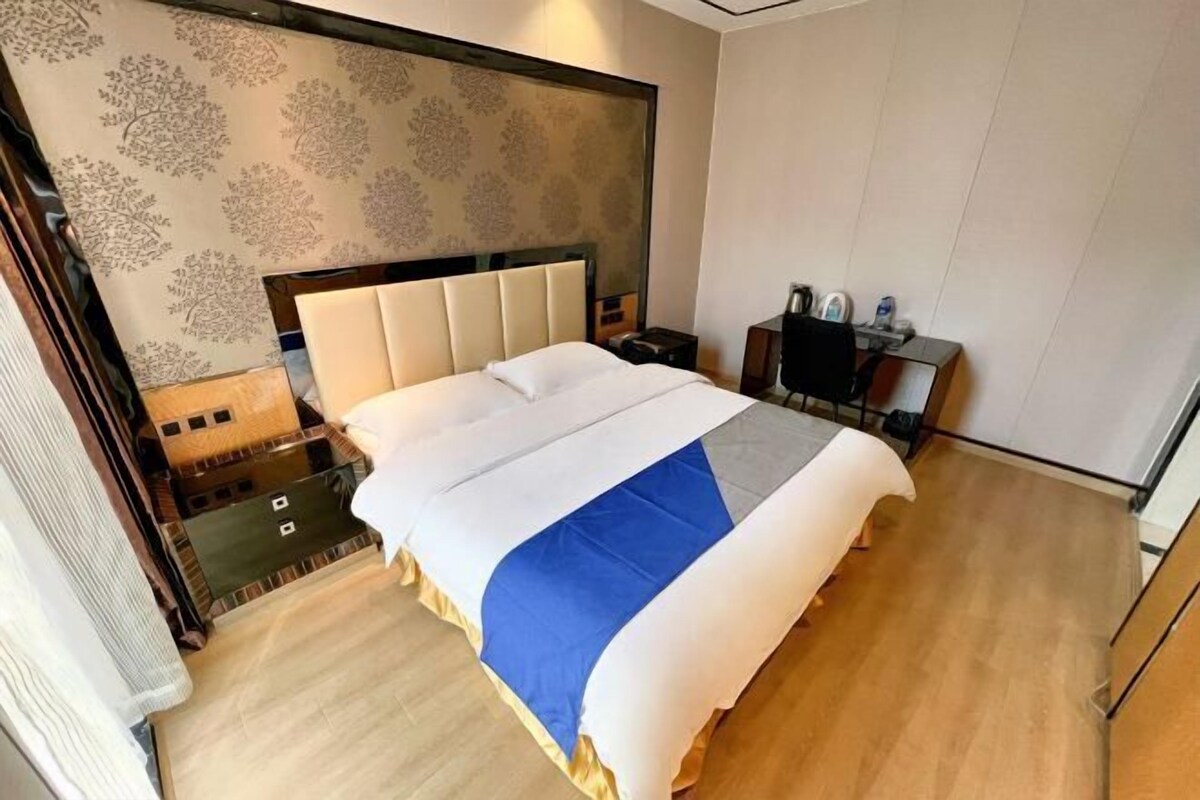 A hotel room with a bed, bedside tables, a desk, and a headboard with a patterned wallpaper.