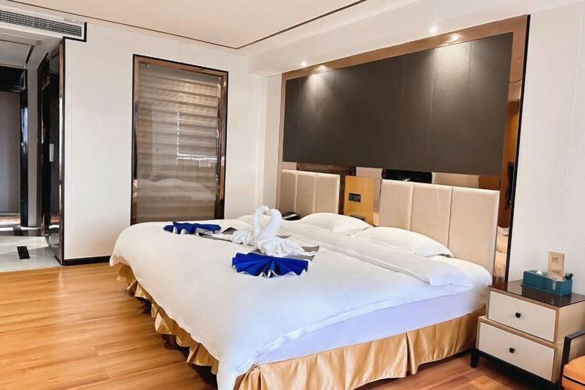 A modern hotel room with a large bed, a wooden headboard, a bedside table, and a wardrobe.