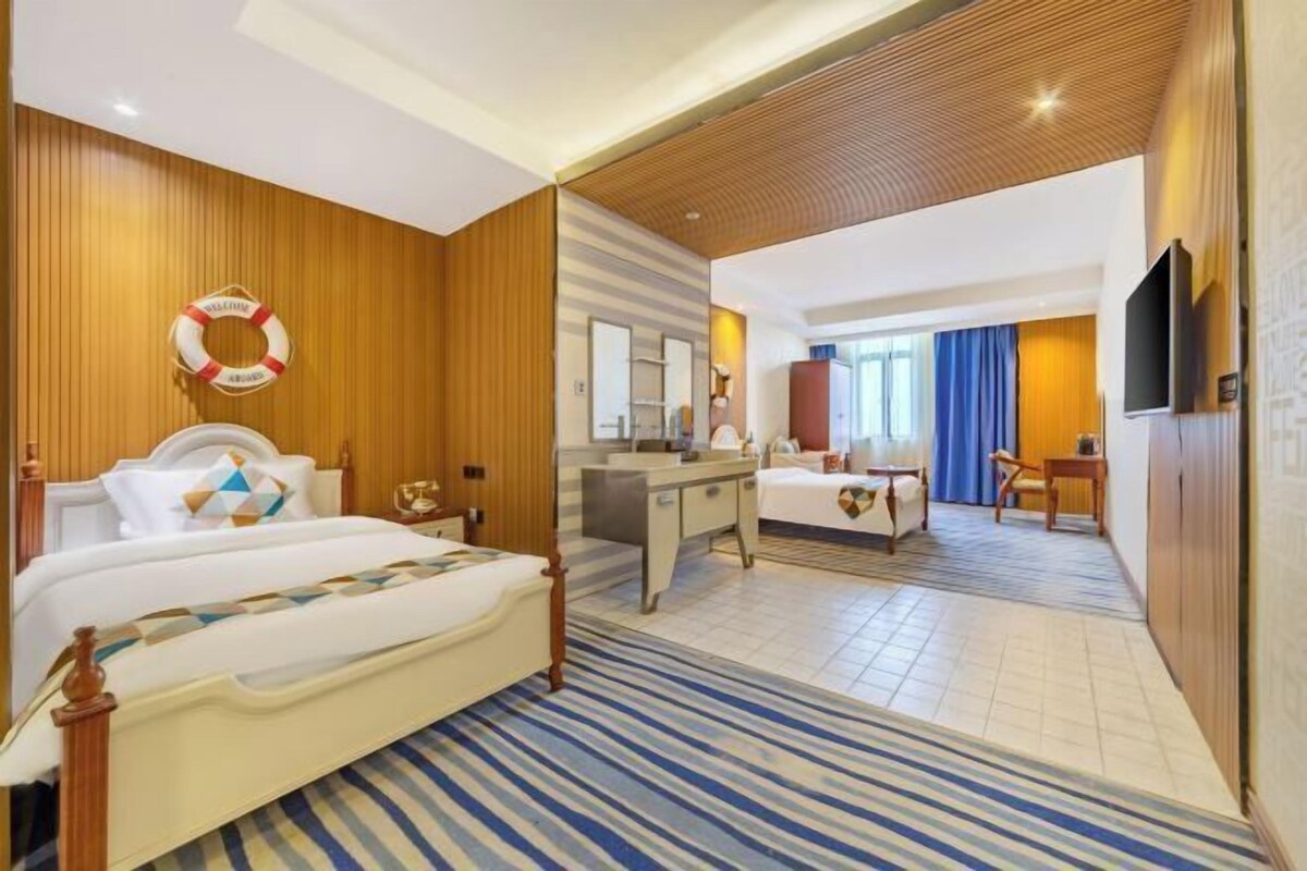 A hotel room with a bed, a desk, a mirror, a life preserver, and a TV.