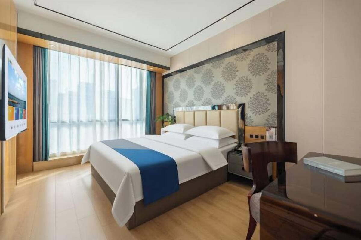 A hotel room with a large bed, a desk, and a view of the city through the window.