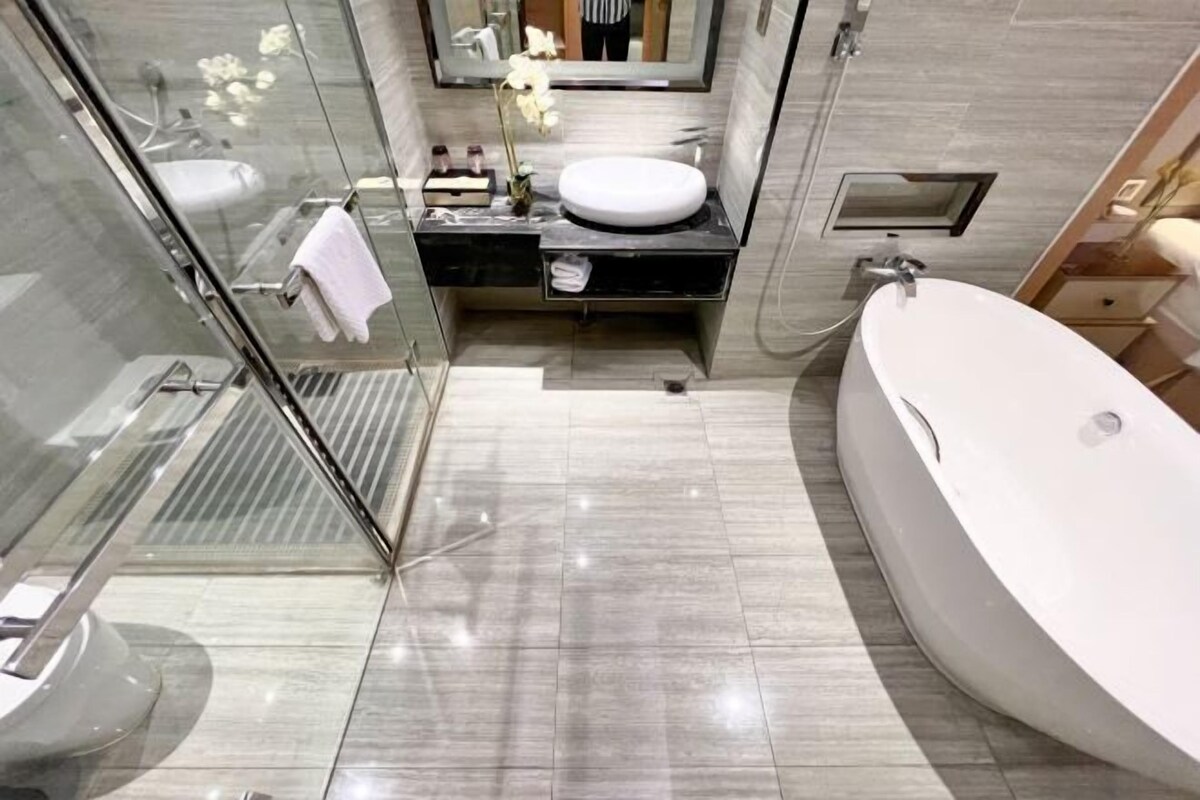 A modern bathroom with a glass shower enclosure, a large freestanding bathtub, and a vanity with a round sink.