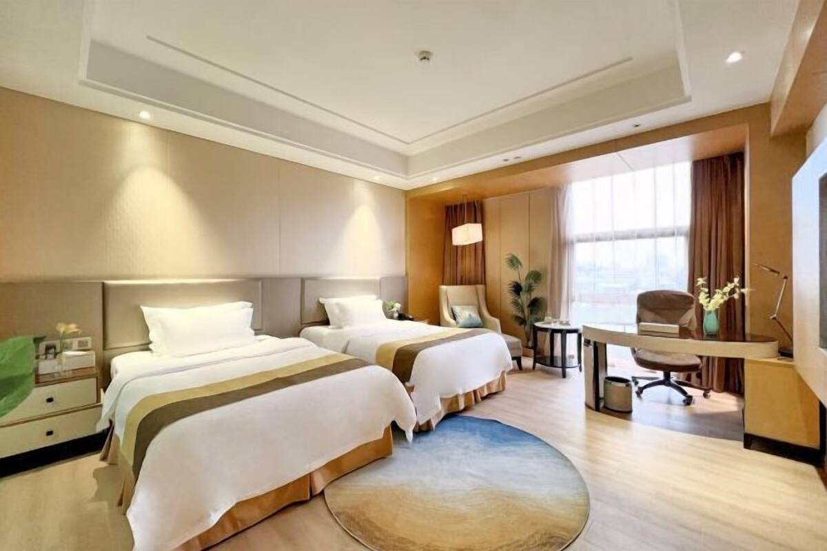 A hotel room with two beds, a desk, a chair, a lamp, and a window with curtains.