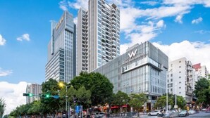A modern high-rise building with a prominent 'W' logo, surrounded by other tall buildings and a clear blue sky. - Sweet World Hotel (Foshan Jihuayuan, Zumiao) (Foshan)