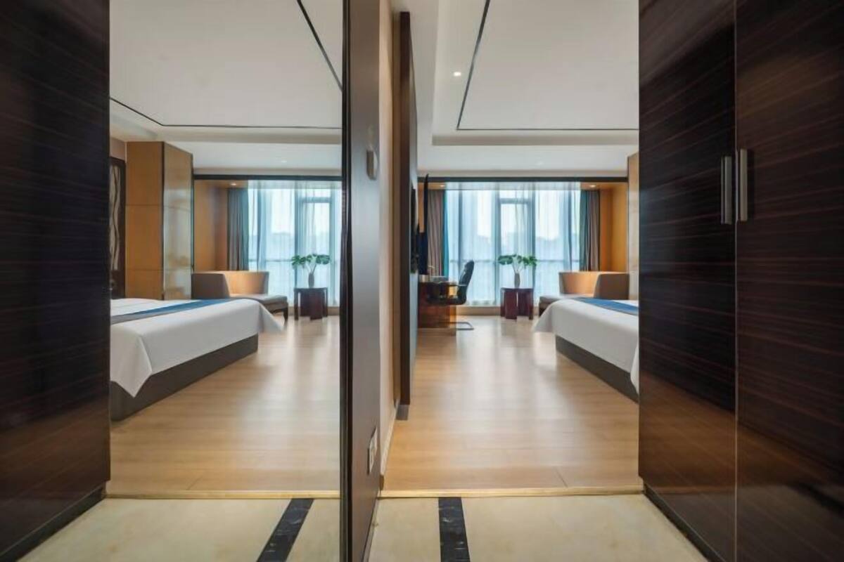 A hotel room with two beds, a desk, and a view of the city.