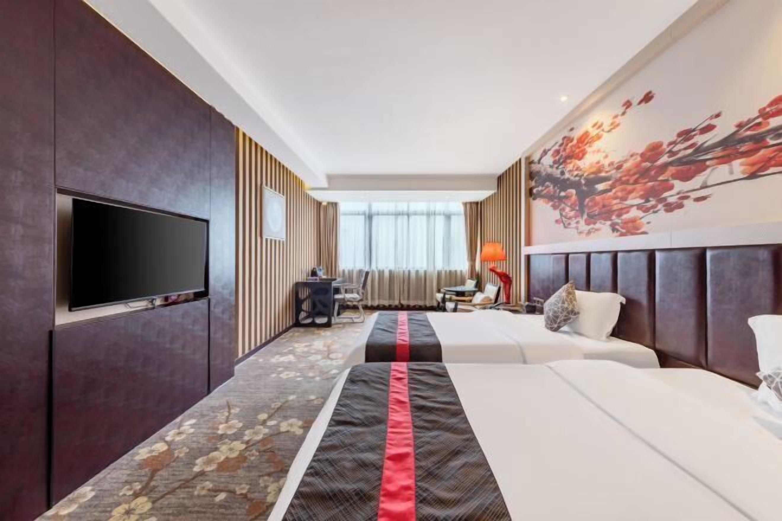 A hotel room with a large flat-screen TV, two beds, a desk, and a chair.