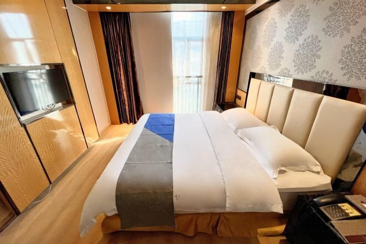 A hotel room with a bed, curtains, a TV, and a patterned wall.