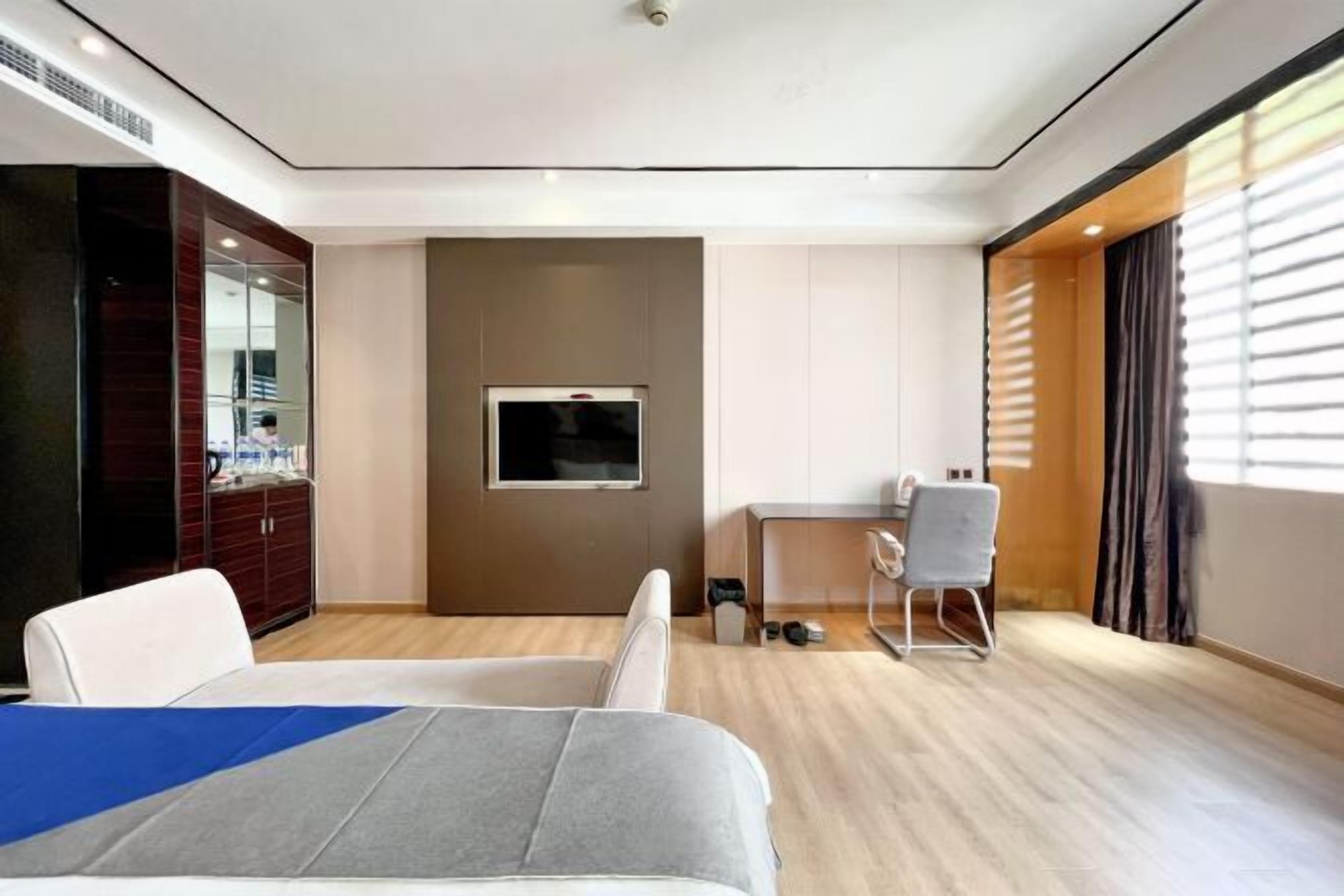 Quarto de hotel com cama, escrivaninha, televisão e guarda-roupa.