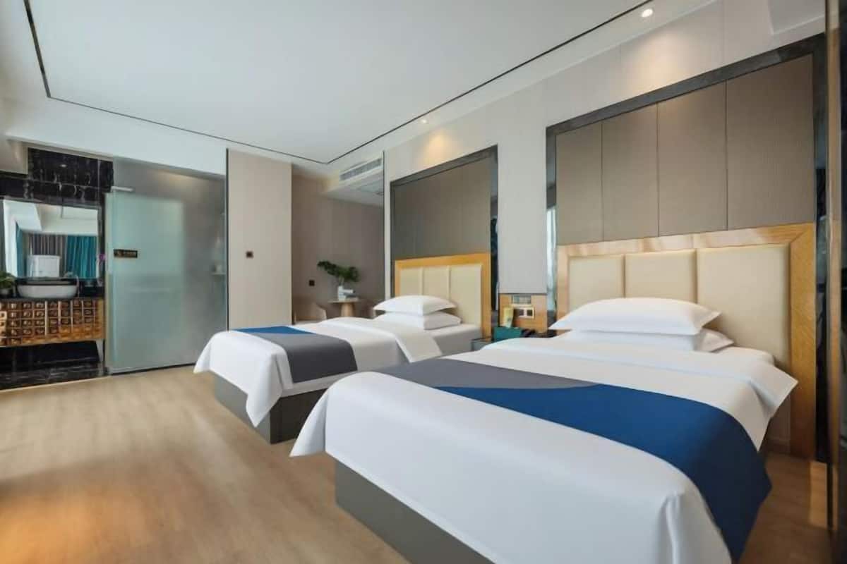 A hotel room with two beds, a mirror, a bedside table, and a small plant.