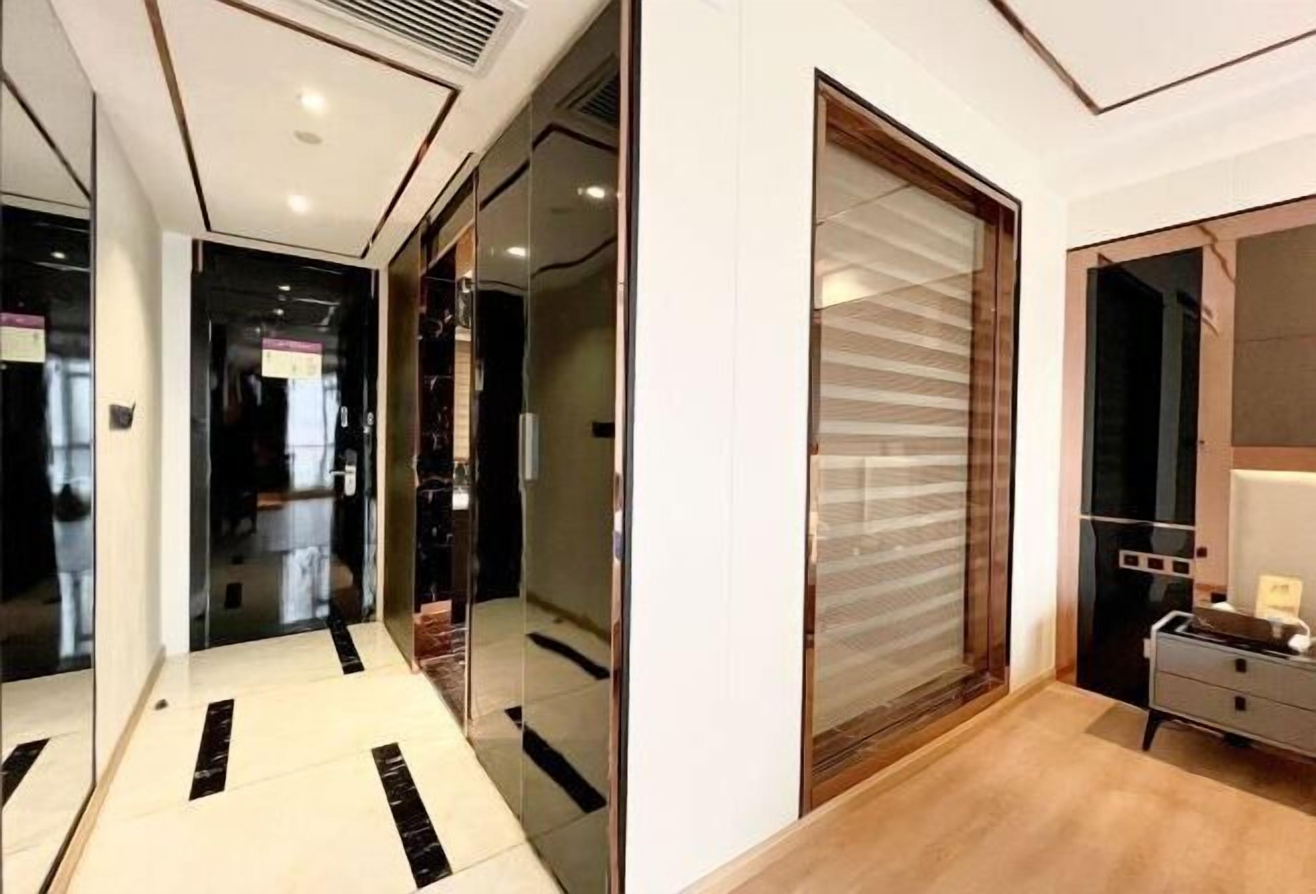 Um corredor moderno com portas de vidro que dão para um quarto com piso de madeira e uma grande janela.