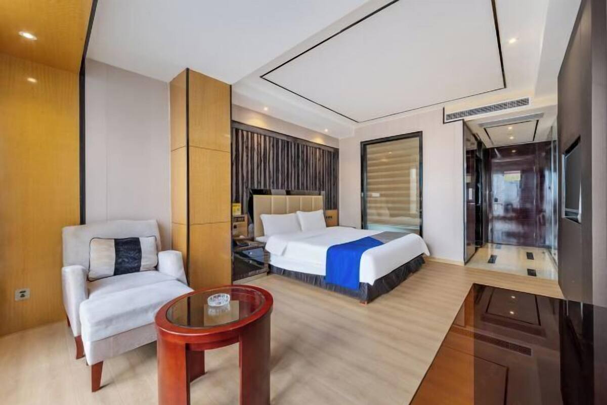 A modern hotel room with a large bed, a seating area with a small table, and a large window.