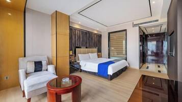A modern hotel room with a large bed, a seating area with a small table, and a large window.