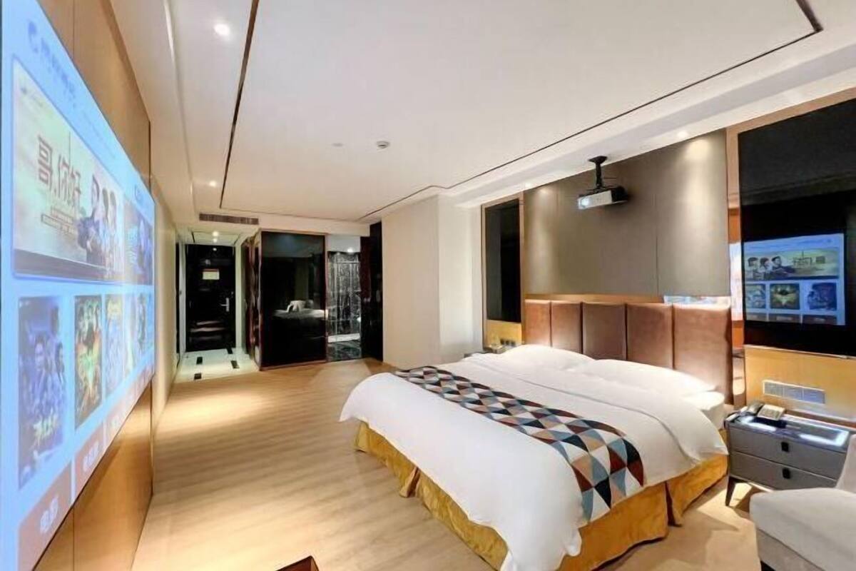 A modern hotel room with a large bed, a television, and a wall-mounted projector screen.