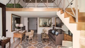 En rummelig opholdsstue med hvælvet loft, trappe, sofa, sofabord og en lænestol.
