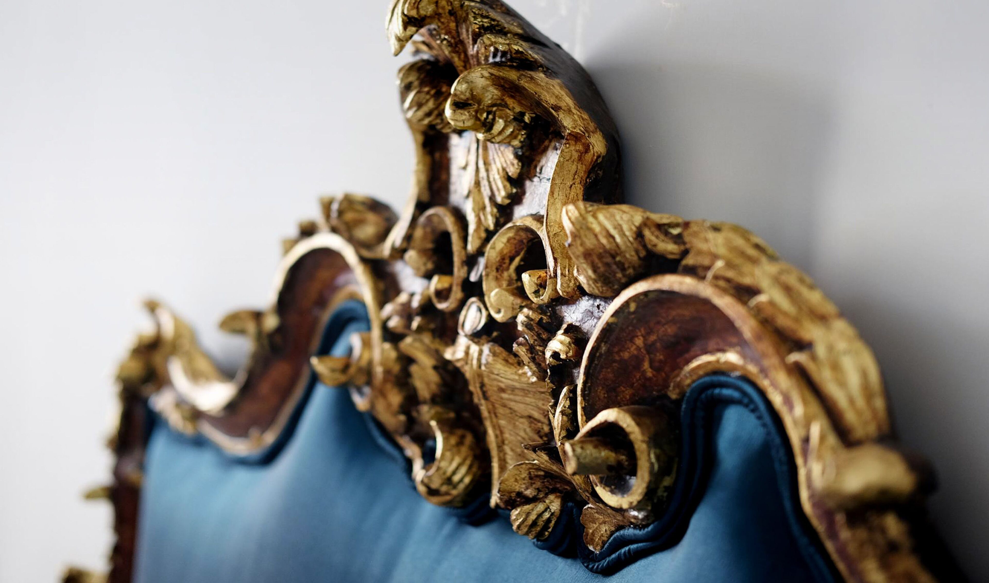 A close-up of an ornate, gold-accented chair with intricate carvings and a blue upholstered seat.