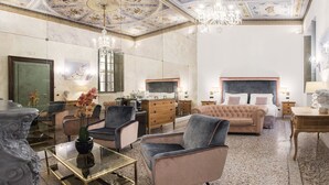 Et luksuriøst hotelværelse med en stor seng, et siddeområde med sofa og stole, et spisebord og en lysekrone.