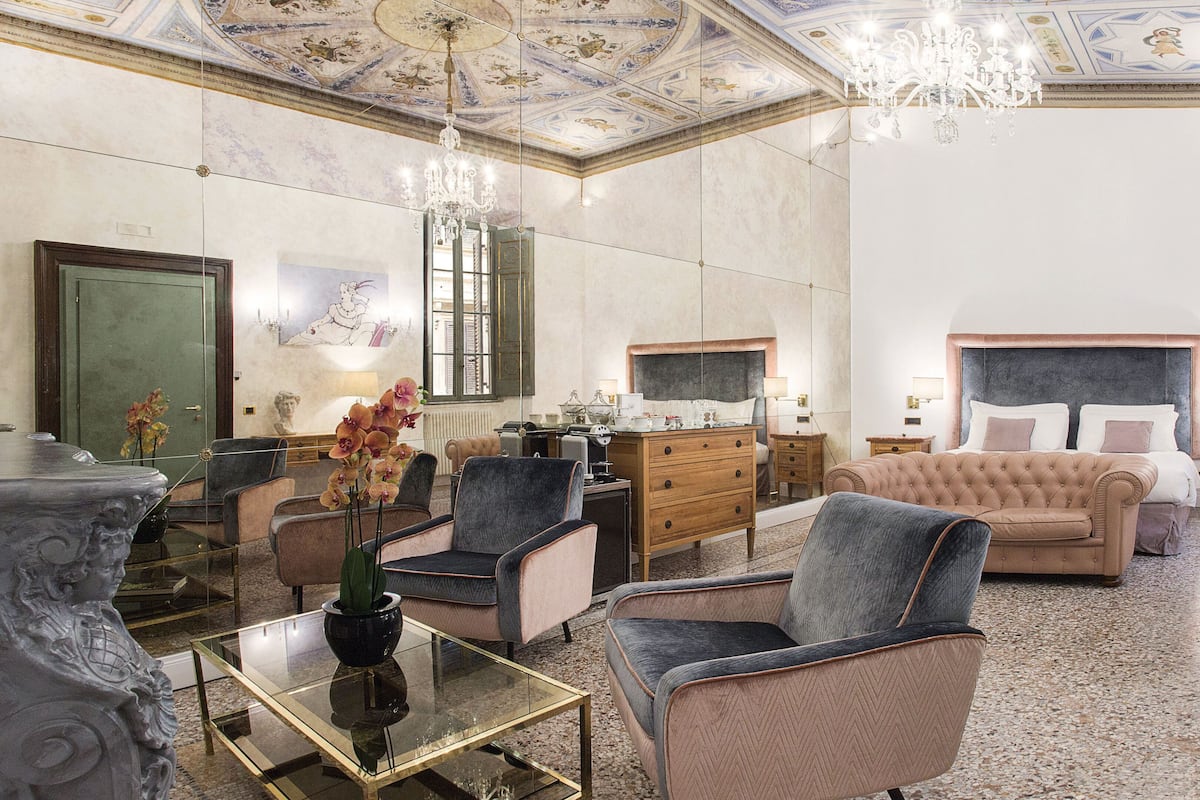 Una lujosa habitación de hotel con una cama grande, una zona de estar con sofá y sillones, una mesa de comedor y un candelabro.