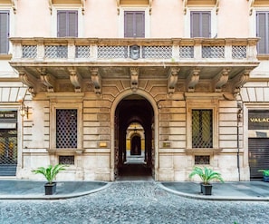 A historic building entrance with an ornate archway, potted plants, and a cobblestone street. - Nobildonne Relais (Rome)