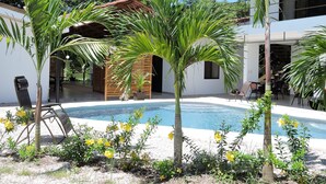 A pool area with palm trees, a wooden structure, and a modern building in the background. - Las Perlitas Boutique Hotel (Sámara)