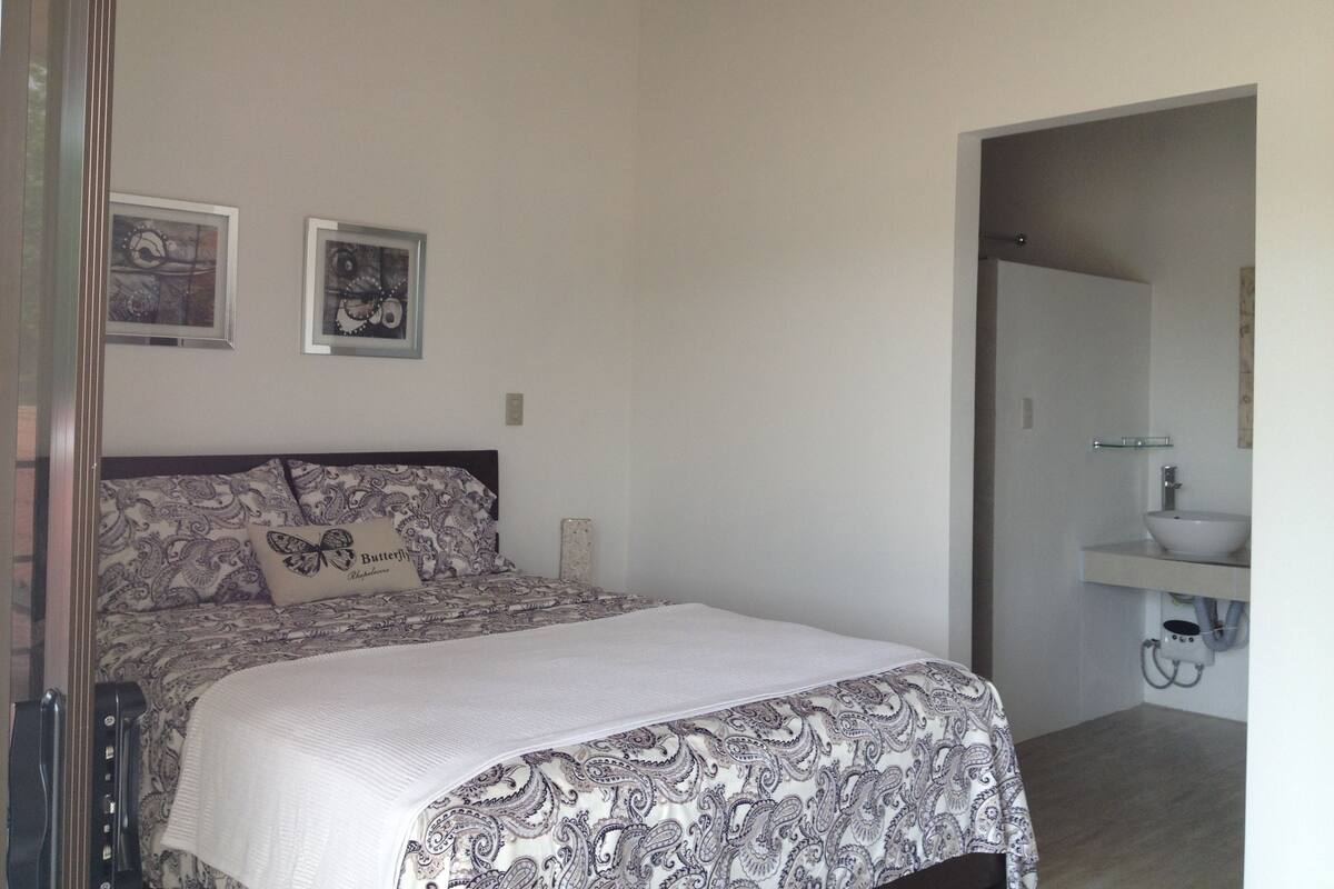 Ein Schlafzimmer mit Bett, Nachttisch, Spiegel und einem durchgehenden Türspalt sichtbaren Badezimmer.