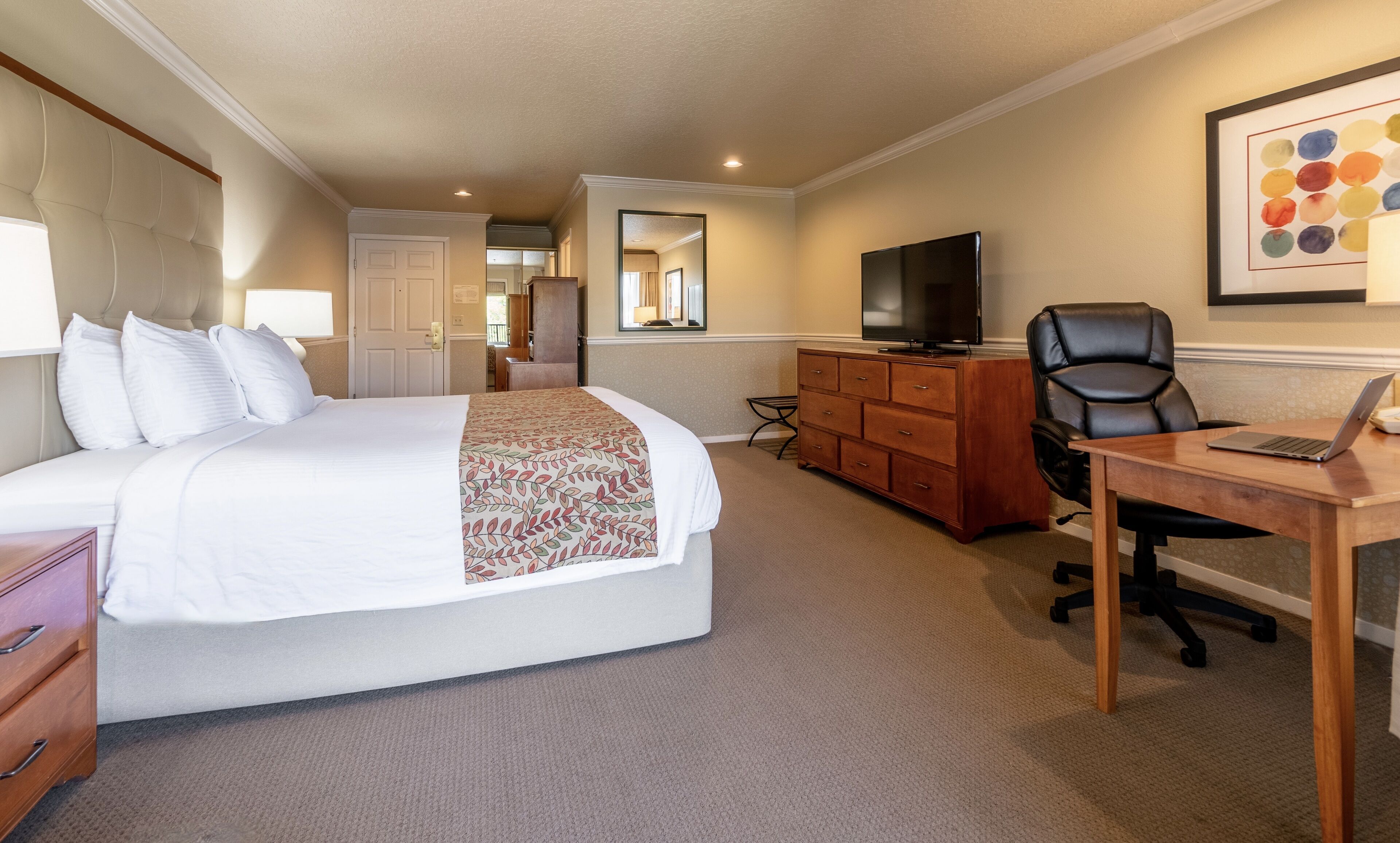 A hotel room with a bed, a desk with a laptop, a television, and a mirror.