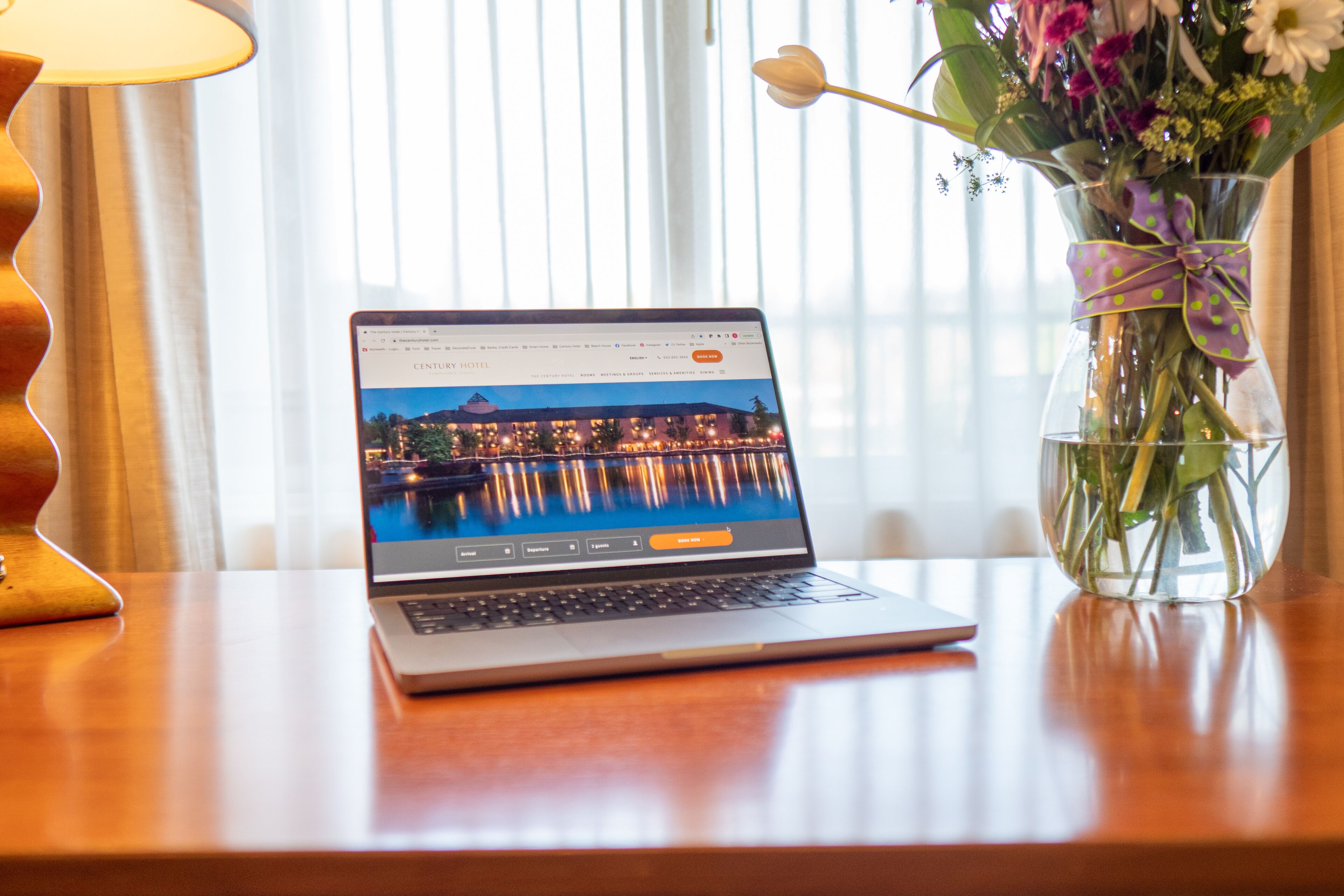 A laptop on a wooden table with a view of a cityscape through the window.