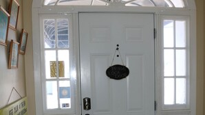 A white door with a sign that says "Please Lock Door." There are framed pictures on the wall to the left and a wooden bench in the foreground.