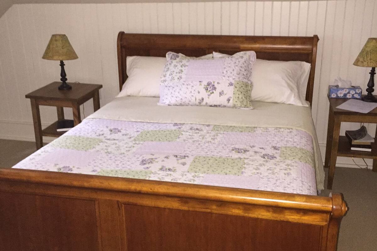 A wooden bed with a floral quilt, two bedside tables with lamps, and a white wall.