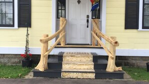 A yellow building with a white door, black shutters, and a wooden staircase leading to the entrance.