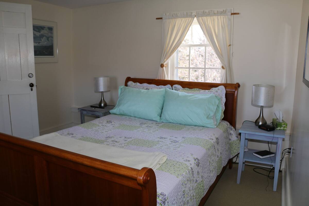 A bedroom with a wooden bed, two bedside tables with lamps, a window with curtains, and a door.