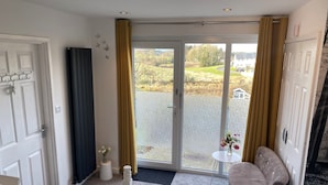 Habitación de hotel con cama, una silla, una mesita con flores, ventana con cortinas y vista al exterior.