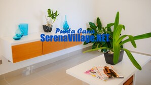 A modern reception area with a white counter, a blue vase, and potted plants. - Serena Village (Punta Cana)