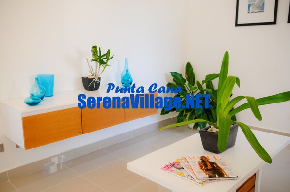 A modern reception area with a white counter, a blue vase, and potted plants. - Serena Village (Punta Cana)