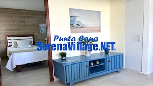 A bedroom with a bed, a nightstand, a dresser, and a painting of a beach scene. - Serena Village (Punta Cana)