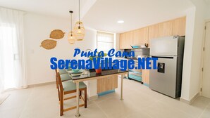 A modern kitchen with wooden cabinets, a stainless steel refrigerator, and a dining area with a table and chairs. - Serena Village (Punta Cana)