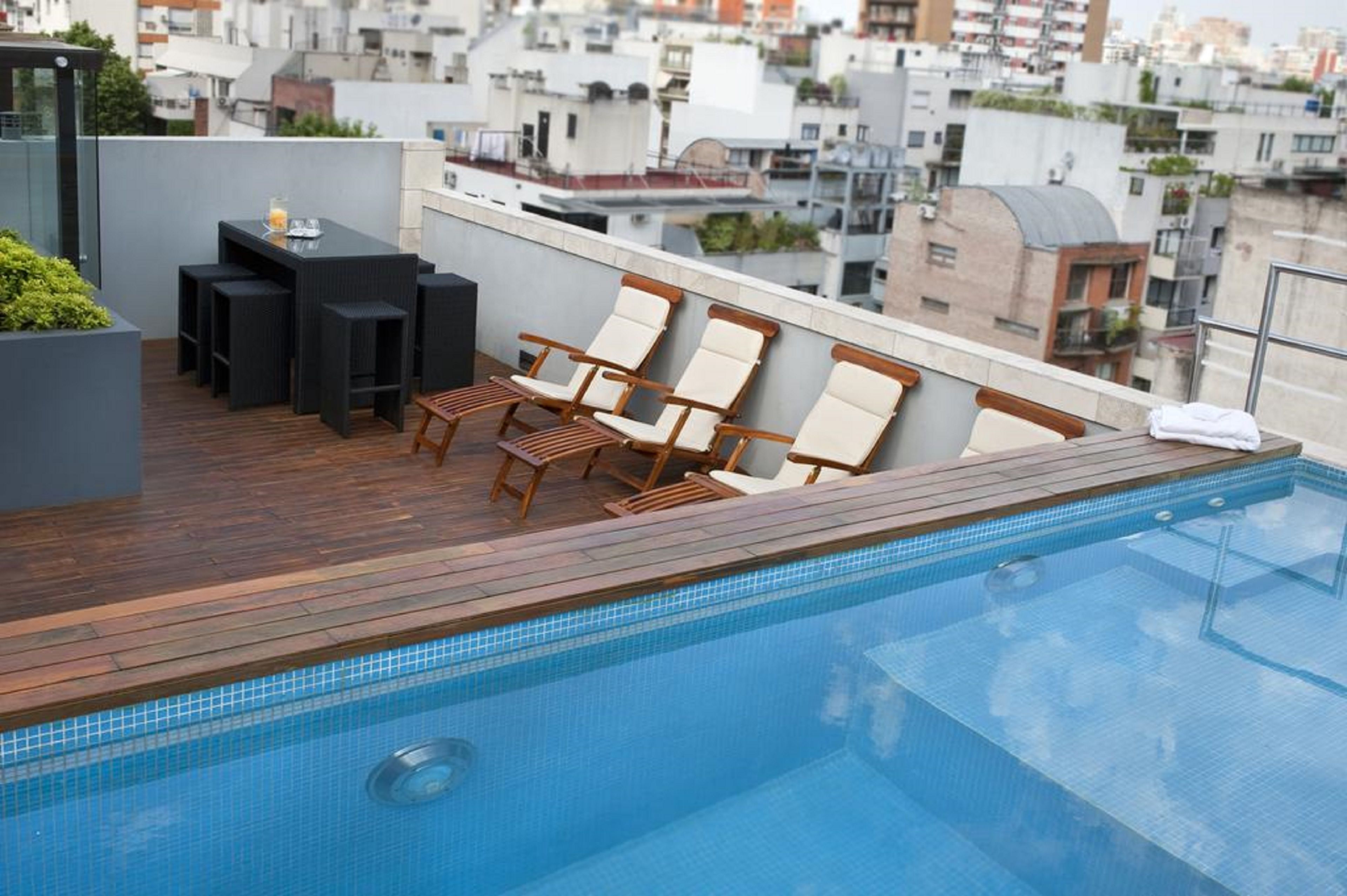 A rooftop pool with wooden deck, lounge chairs, and a bar area.