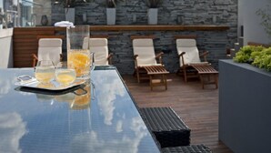 Una terraza en la azotea con una mesa de vidrio, dos vasos de jugo de naranja y cuatro sillones reclinables.