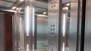 Un ascensor con paredes metálicas, un panel de control con botones y un suelo estampado.