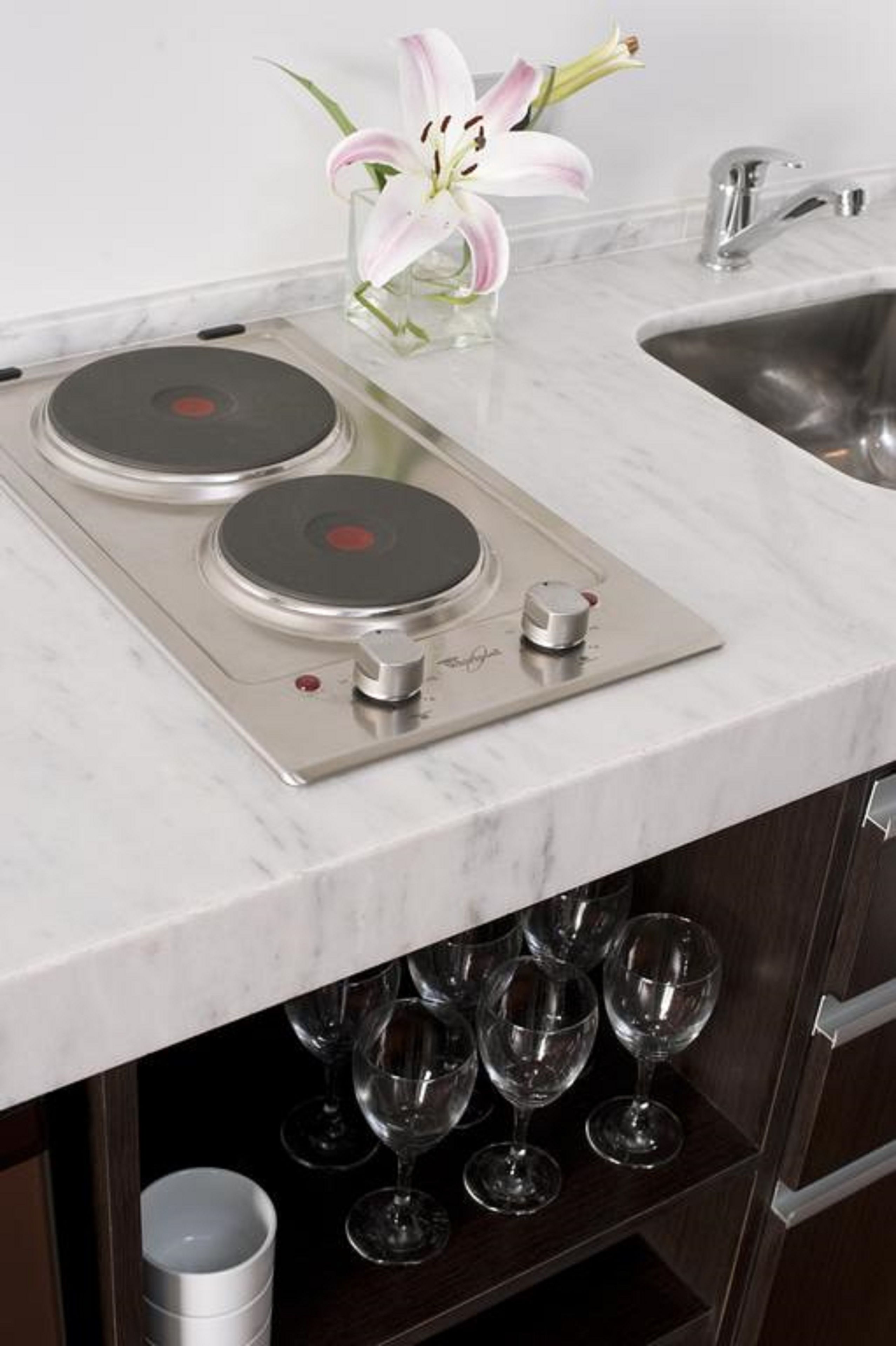 Una cocina con placa de inducción integrada, un lavamanos y una estantería para vinos con varias copas.