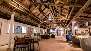 Un espacio interior amplio con techo alto, vigas de madera y una zona de estar con sillas y sofás.
