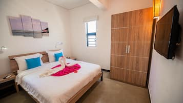 Una habitación de hotel con cama, armario, televisor montado en la pared y ventana.