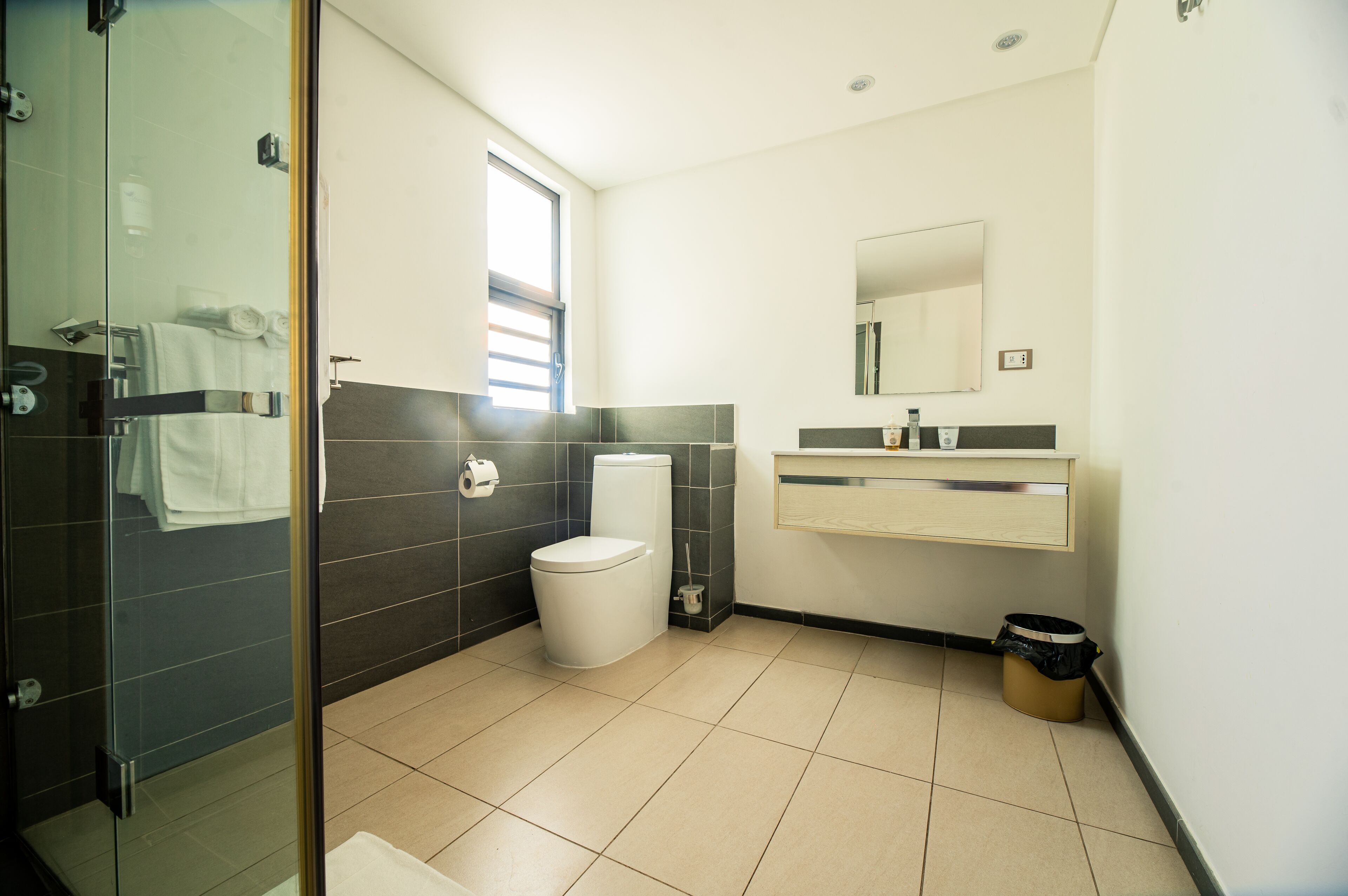 Une salle de bain moderne avec une douche à parois de verre, des toilettes, un lavabo avec un miroir et une poubelle.