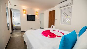 A hotel room with a bed, a TV, a wall-mounted air conditioner, and a window with a decorative light.