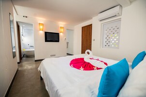 Habitación de hotel con cama, televisor, aire acondicionado de pared y ventana con luz decorativa.