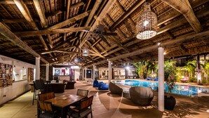 Zona de piscina interior con vigas de madera, asientos y ventilador de techo.