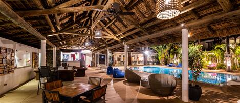 Un espace piscine intérieur avec des poutres en bois, des sièges et un ventilateur de plafond.