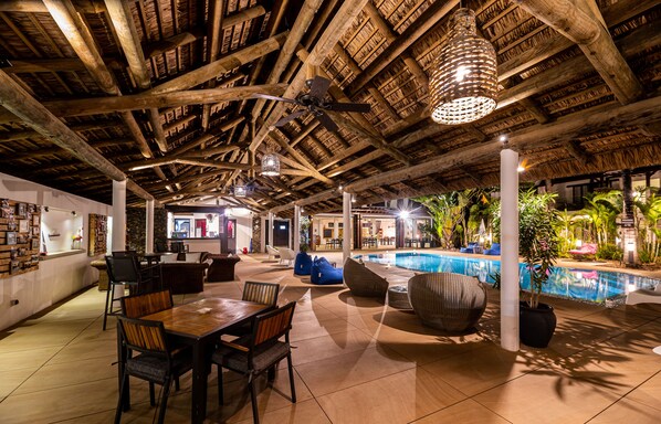 An indoor pool area with wooden beams, seating, and a ceiling fan.