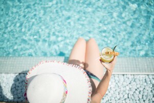 A person relaxing by a pool with a drink in hand.
